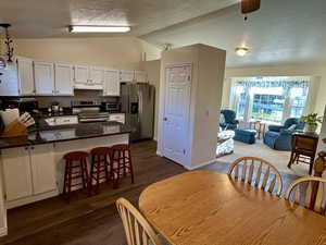 Dining room with a textured ceiling, lofted ceiling, and dark wood-style flooring