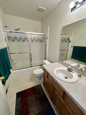 Full bath with a textured ceiling, vanity, enclosed tub / shower combo, and dark tile patterned flooring
