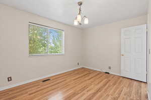 Empty room with light wood-type flooring and a chandelier
