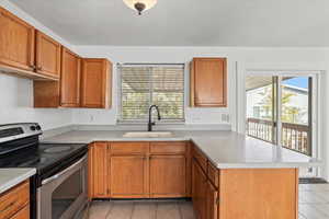 Kitchen featuring stainless steel electric range oven, a peninsula, brown cabinets, and light tile patterned floors