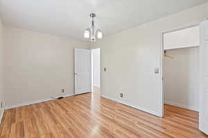 Unfurnished bedroom with a walk in closet, light wood finished floors, and a chandelier