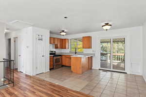 Kitchen featuring light countertops, stainless steel electric range, brown cabinets, light tile patterned flooring, and a peninsula