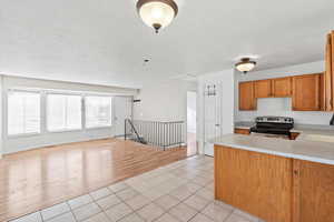 Kitchen featuring light tile patterned floors, stainless steel electric range oven, brown cabinetry, open floor plan, and a peninsula
