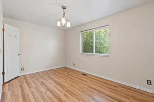 Unfurnished room with light wood-type flooring and a chandelier