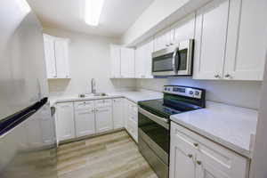 Kitchen with appliances with stainless steel finishes, light countertops, white cabinets, light wood-type flooring, and a textured ceiling