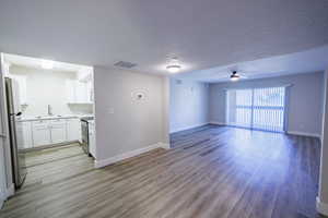 Unfurnished living room with a textured ceiling, light wood-style floors, and ceiling fan