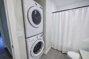 Bathroom with a shower with curtain, stacked washer / drying machine, and tile patterned flooring