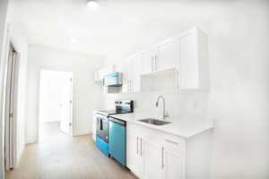 Kitchen with white cabinetry, stainless steel appliances, light wood-style floors, and light stone countertops
