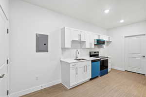 Entrance opens to kitchen with white cabinetry, range with electric stovetop, electric panel, light wood finished floors, and dishwashing machine
