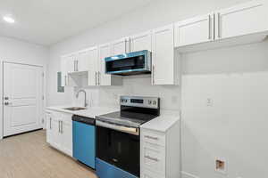 Kitchen with stainless steel appliances, white cabinets, and light wood-style floors