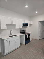 Kitchen with white cabinets, range with electric stovetop, stainless steel microwave, recessed lighting, and light wood-type flooring