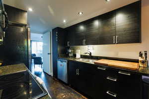 Kitchen featuring stainless steel dishwasher, dark stone countertops, dark cabinetry, range with electric stovetop, and freestanding refrigerator