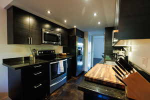 Kitchen with dark cabinets, stainless steel appliances, concrete flooring, dark stone countertops, and recessed lighting