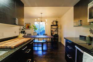 Kitchen featuring dark cabinets, dark stone countertops, a chandelier, and stainless steel microwave