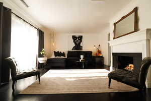 Living area with a warm lit fireplace, ornamental molding, and wood finished floors