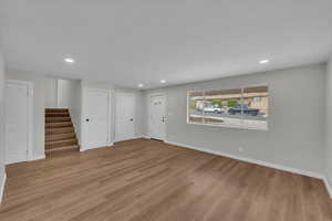 Unfurnished living room featuring recessed lighting, light wood-style flooring, and stairway