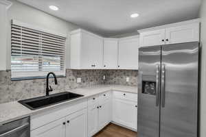 Kitchen with stainless steel appliances, white cabinetry, light stone countertops, backsplash, and recessed lighting