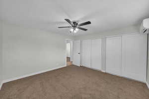 Unfurnished bedroom with multiple closets, carpet flooring, a wall mounted AC, and ceiling fan