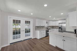 Kitchen with french doors, white cabinetry, stainless steel appliances, light stone counters, and dark wood-style floors