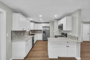 Kitchen with a peninsula, white cabinets, appliances with stainless steel finishes, light stone countertops, and recessed lighting