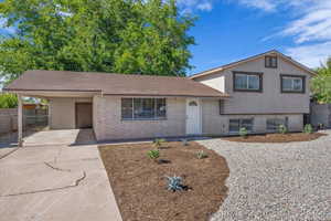 Tri-level home with brick siding, an attached carport, concrete driveway, and stucco siding