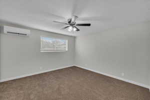 Unfurnished room featuring carpet, a wall unit AC, and a ceiling fan