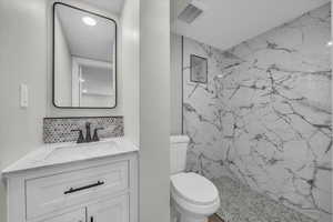 Bathroom featuring vanity, a marble finish shower, tasteful backsplash, and recessed lighting