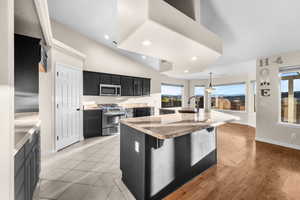 Kitchen featuring dark cabinetry, recessed lighting, pendant lighting, a kitchen island with sink, and appliances with stainless steel finishes