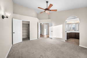 Unfurnished bedroom with carpet, a spacious closet, high vaulted ceiling, ceiling fan, and arched walkways
