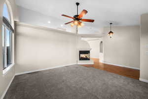 Unfurnished living room featuring carpet flooring, a multi sided fireplace, lofted ceiling, ceiling fan, and recessed lighting