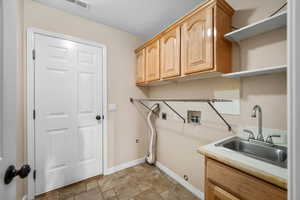 Washroom featuring cabinet space, hookup for a washing machine, hookup for an electric dryer, and stone finish floors