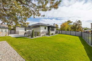 Rear view of property featuring stone siding, a chimney, a fenced backyard, stucco siding, and a patio