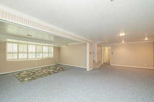 Unfurnished basement room featuring ornamental molding, carpet flooring, stairway, and wooden walls