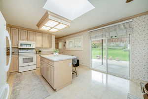 Kitchen with white appliances, wallpapered walls, light brown cabinets, a kitchen island, and a kitchen breakfast bar