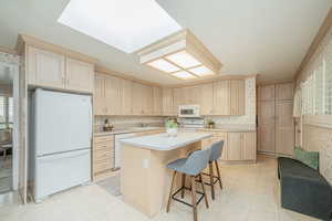 Kitchen with wallpapered walls, white appliances, a breakfast bar, light countertops, and a kitchen island