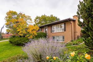 View of property exterior with a chimney, brick siding, and a lawn