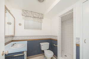 Full bathroom featuring light tile patterned floors, tile walls, vanity, a shower stall, and a wainscoted wall