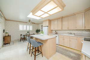 Kitchen featuring light brown cabinetry, wallpapered walls, light countertops, crown molding, and ceiling fan