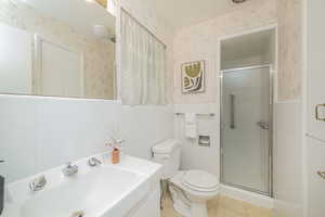 Bathroom featuring wallpapered walls, vanity, a stall shower, light tile patterned floors, and tile walls