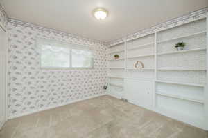 Empty room with light carpet, wallpapered walls, and built in features