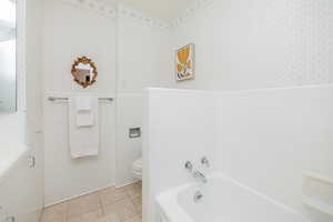 Full bath with a bath, light tile patterned floors, tile walls, and wainscoting