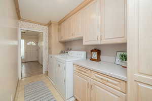 Laundry room featuring cabinet space, wallpapered walls, ornamental molding, separate washer and dryer, and light patterned floors