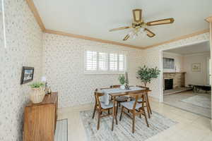 Dining room with crown molding, a fireplace, ceiling fan, wallpapered walls, and light tile patterned flooring