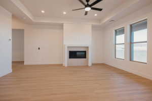 Unfurnished living room featuring a fireplace, light wood-style flooring, recessed lighting, a tray ceiling, and a ceiling fan