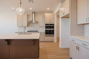 Kitchen with tasteful backsplash, pendant lighting, wall chimney range hood, double oven, and recessed lighting
