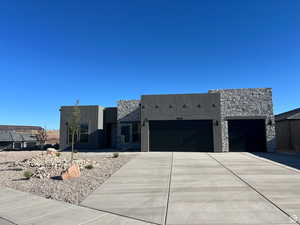 Contemporary home featuring stone siding, stucco siding, a garage, and driveway