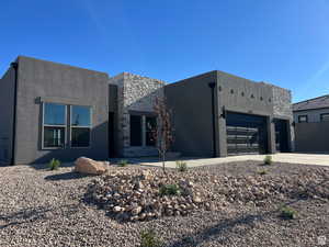 View of front of home with stone siding, driveway, stucco siding, and a garage