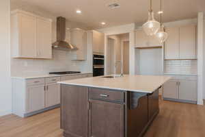 Kitchen featuring decorative backsplash, wall chimney exhaust hood, a kitchen island with sink, pendant lighting, and recessed lighting