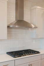 Kitchen with wall chimney range hood, stainless steel gas cooktop, tasteful backsplash, and white cabinets