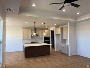 Kitchen featuring pendant lighting, a kitchen island with sink, decorative backsplash, wall chimney range hood, and dark wood-type flooring